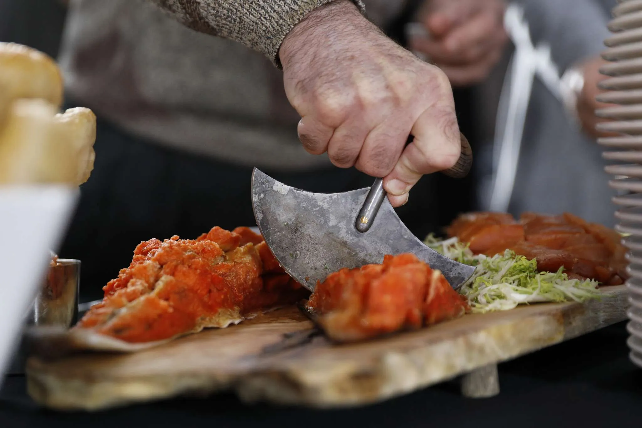 Close-up of hands slicing traditional Inuit food with an ulu knife on a wooden board