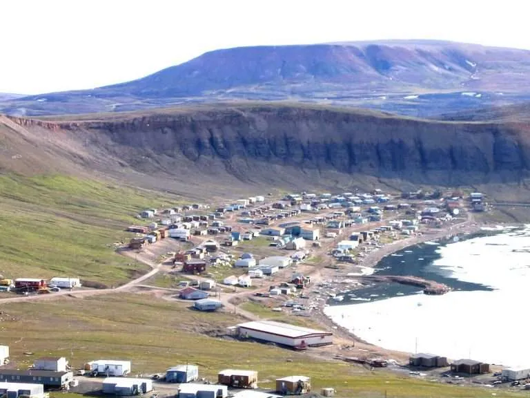 A small Arctic community with houses nestled against a rugged hillside by the shoreline