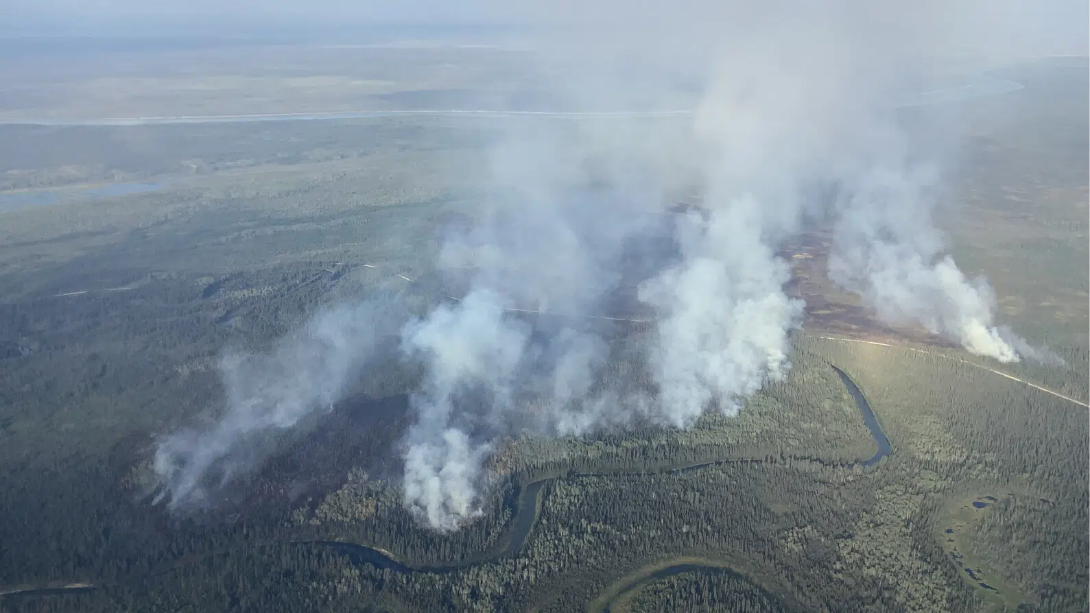 Aerial view of a wildfire burning near Jean Marie River in the Northwest Territories, with smoke rising from multiple areas of the forest.